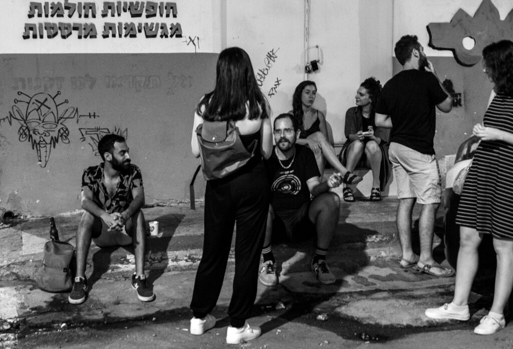 קהל בחצר בשחור־לבן, יושבים ועומדים ליד קיר גרפיטי